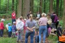 Eltern und Kinder stehen im Halbkreis um einen Förster im Wald